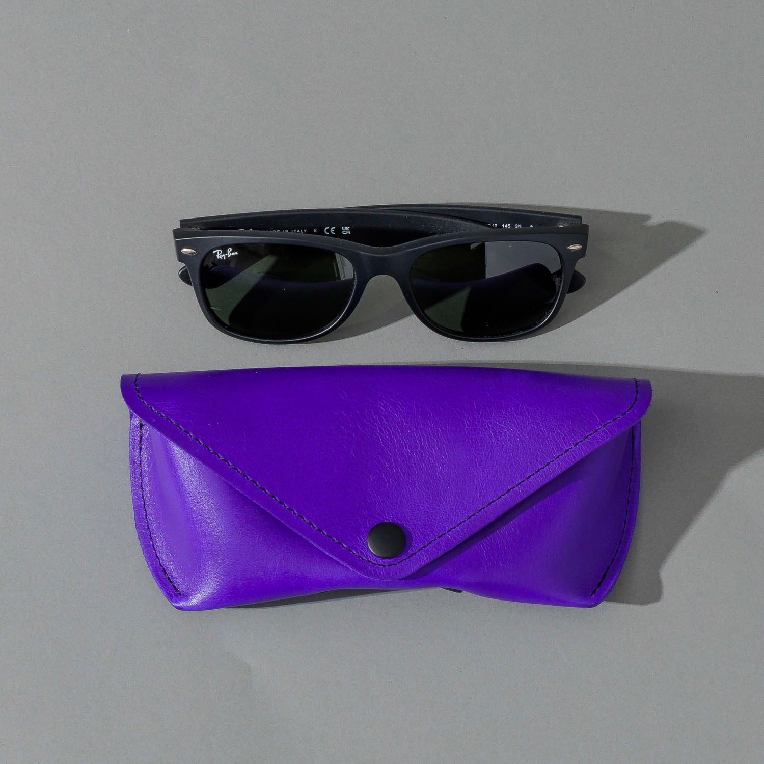 Glasses Case in Violet Latigo, next to a pair of sunglasses, shot 2