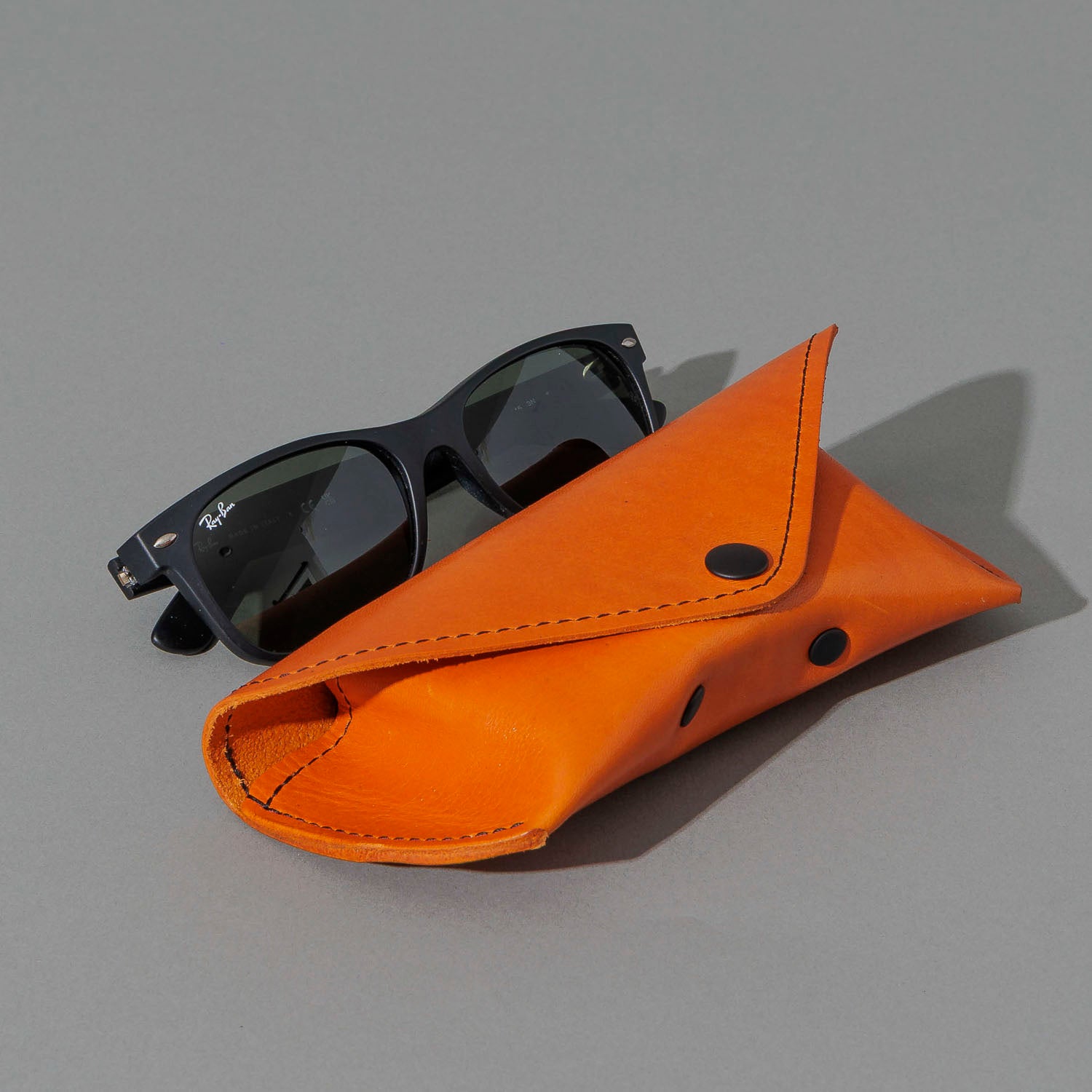 Glasses Case in Orange Latigo, next to a pair of sunglasses, shot 1