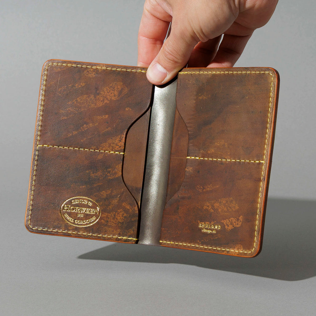 One-Off Traveler Passport Holder in Epic Splatter Reverse Cigar Shell Cordovan, No Bill Slot, held open in hand, shot 2