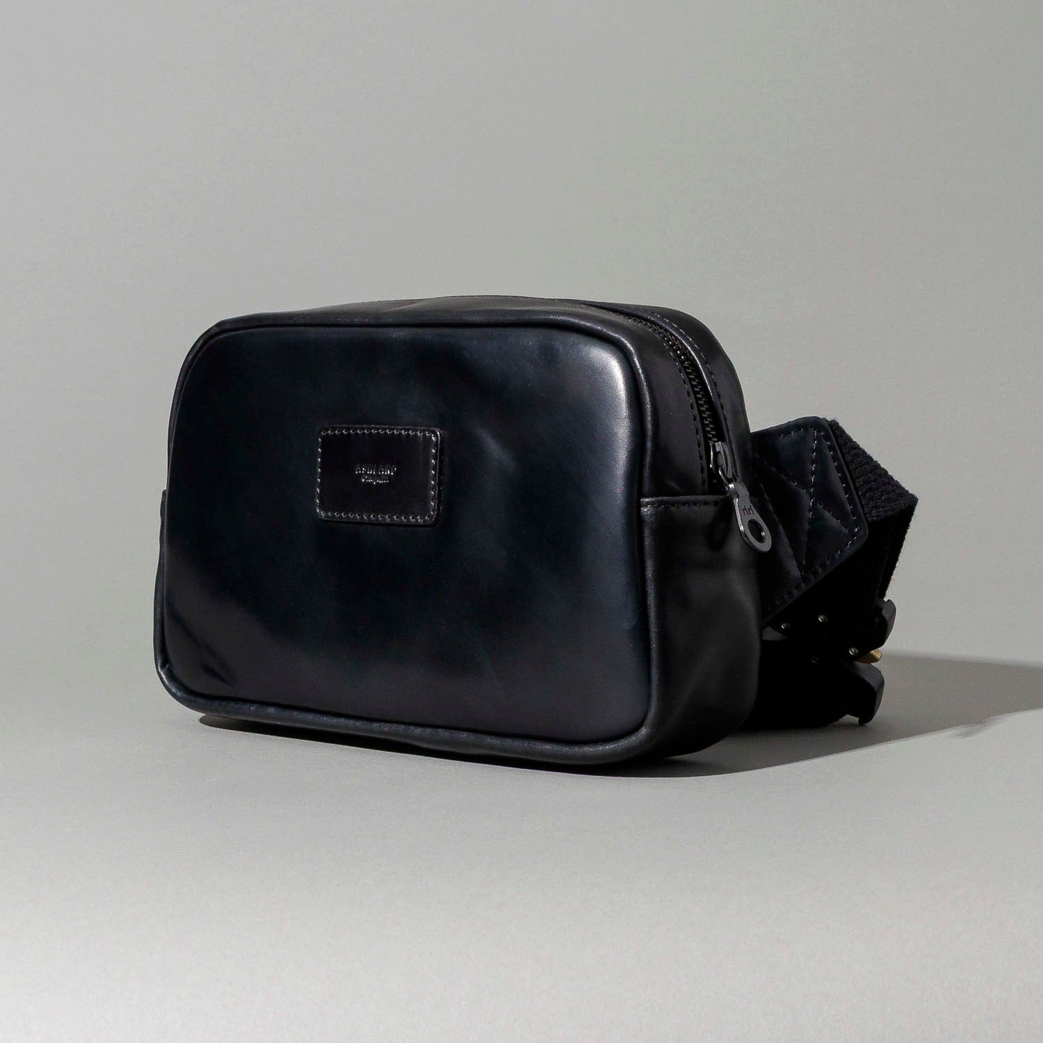 Ashland Leather black Shell Cordovan Sling Bag, front three-quarter view showing brand plaque and adjustable strap