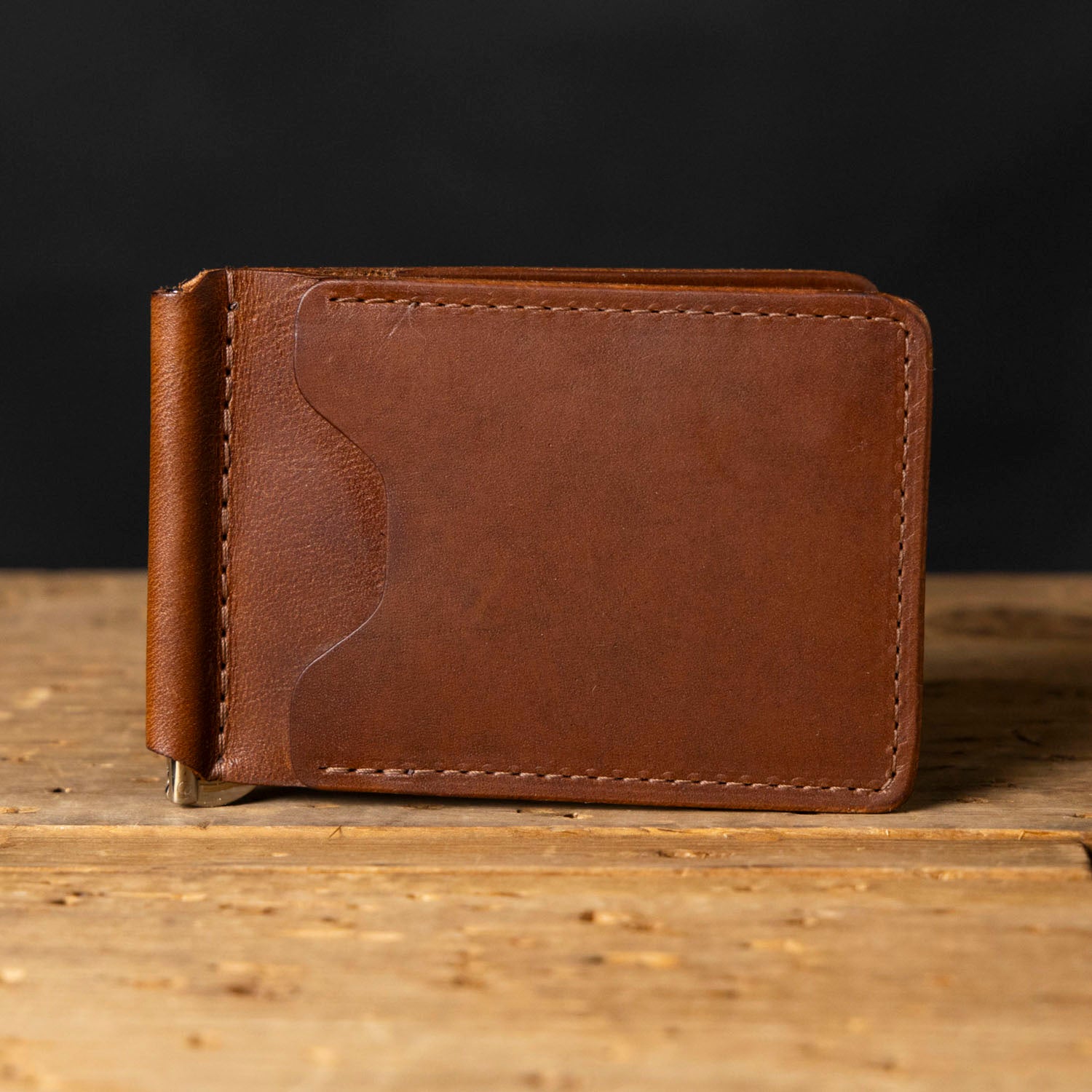Brown leather money clip on a wooden surface with a dark background
