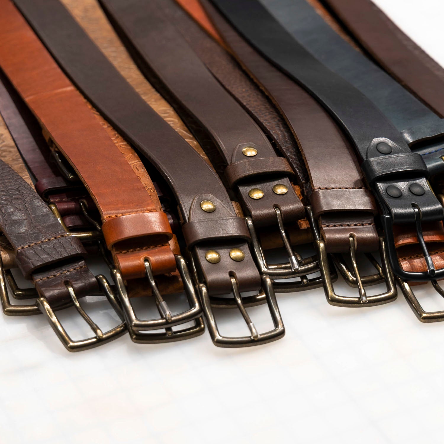 Collection of leather belts in various colors with metal buckles on a white background