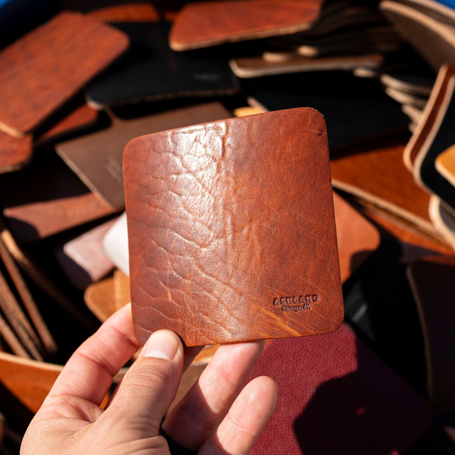 Hand holding a natural leather coaster with embossed branding against a background of other Horween leather coasters