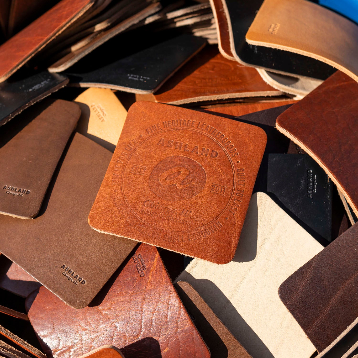Collection of leather coasters with a visible brand logo on a textured surface.