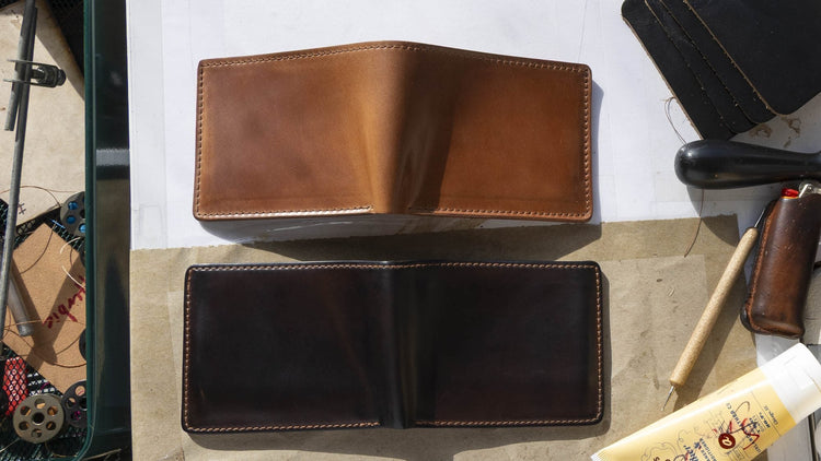 A newer light tan Horween® Shell Cordovan bifold above an aged, deeply darkened shell cordovan bifold on the Ashland Leather workbench