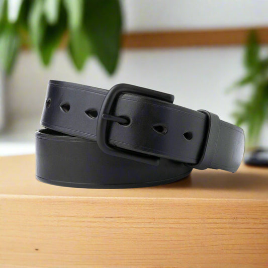 Black leather belt with a large buckle on a wooden desk with plants in the background