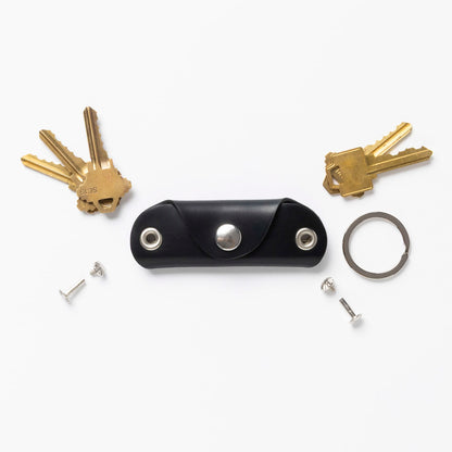 Black leather key holder with keys and tools on a white background
