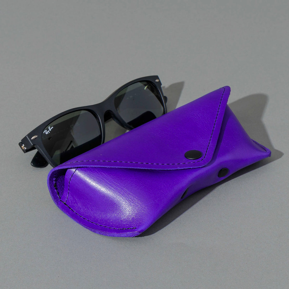 Glasses Case in Violet Latigo, next to a pair of sunglasses, shot 1