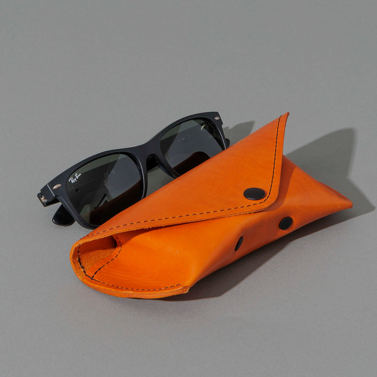 Glasses Case in Orange Latigo, next to a pair of sunglasses, shot 1