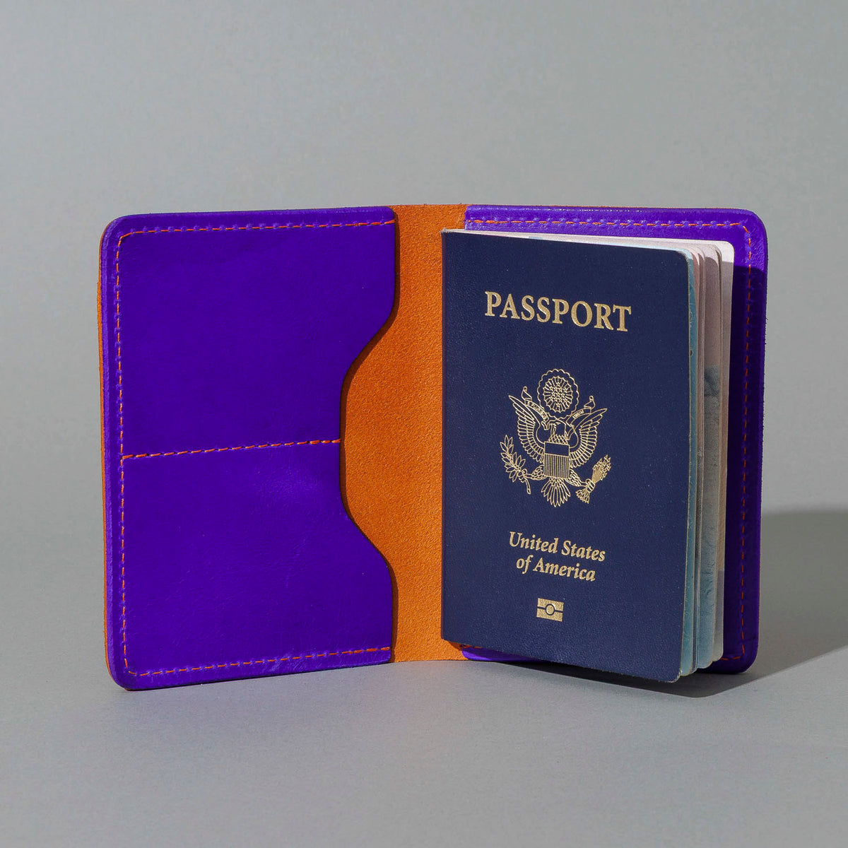 Traveler Passport Holder in Orange Latigo Exterior, Violet Latigo Interior, open with a passport inside, shot 1