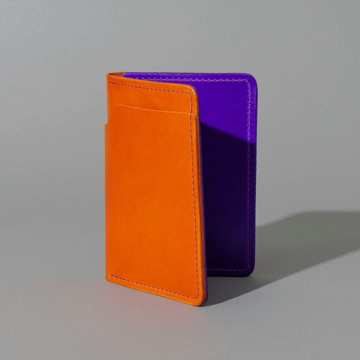 Traveler Passport Holder in Orange Latigo Exterior, Violet Latigo Interior, standing upright, side angle, shot 2