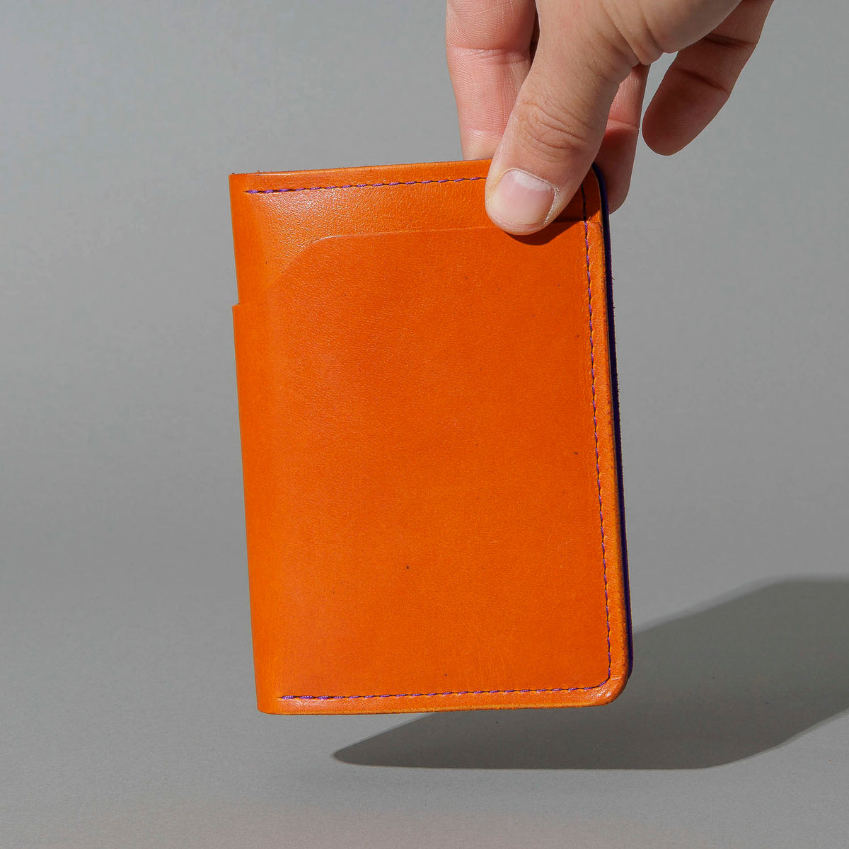 Traveler Passport Holder in Orange Latigo Exterior, Violet Latigo Interior, held in hand, shot 1