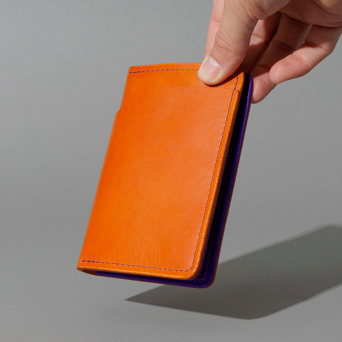 Traveler Passport Holder in Orange Latigo Exterior, Violet Latigo Interior, held in hand, shot 2