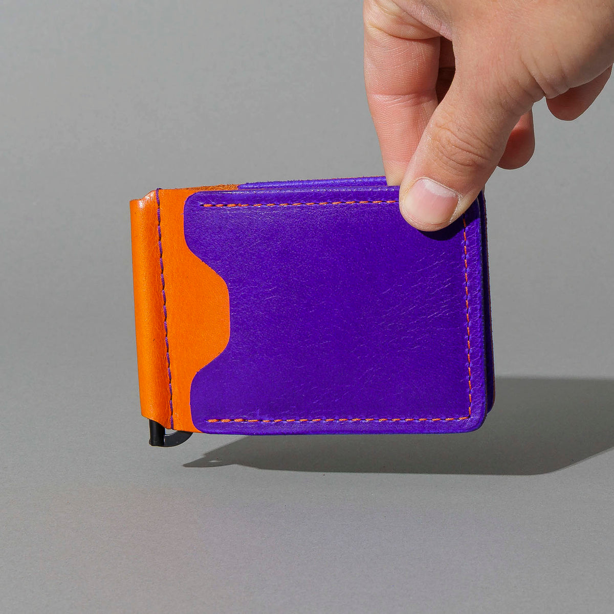 One-Off Capone Money Clip in Violet on Orange Latigo, held in hand, shot 1