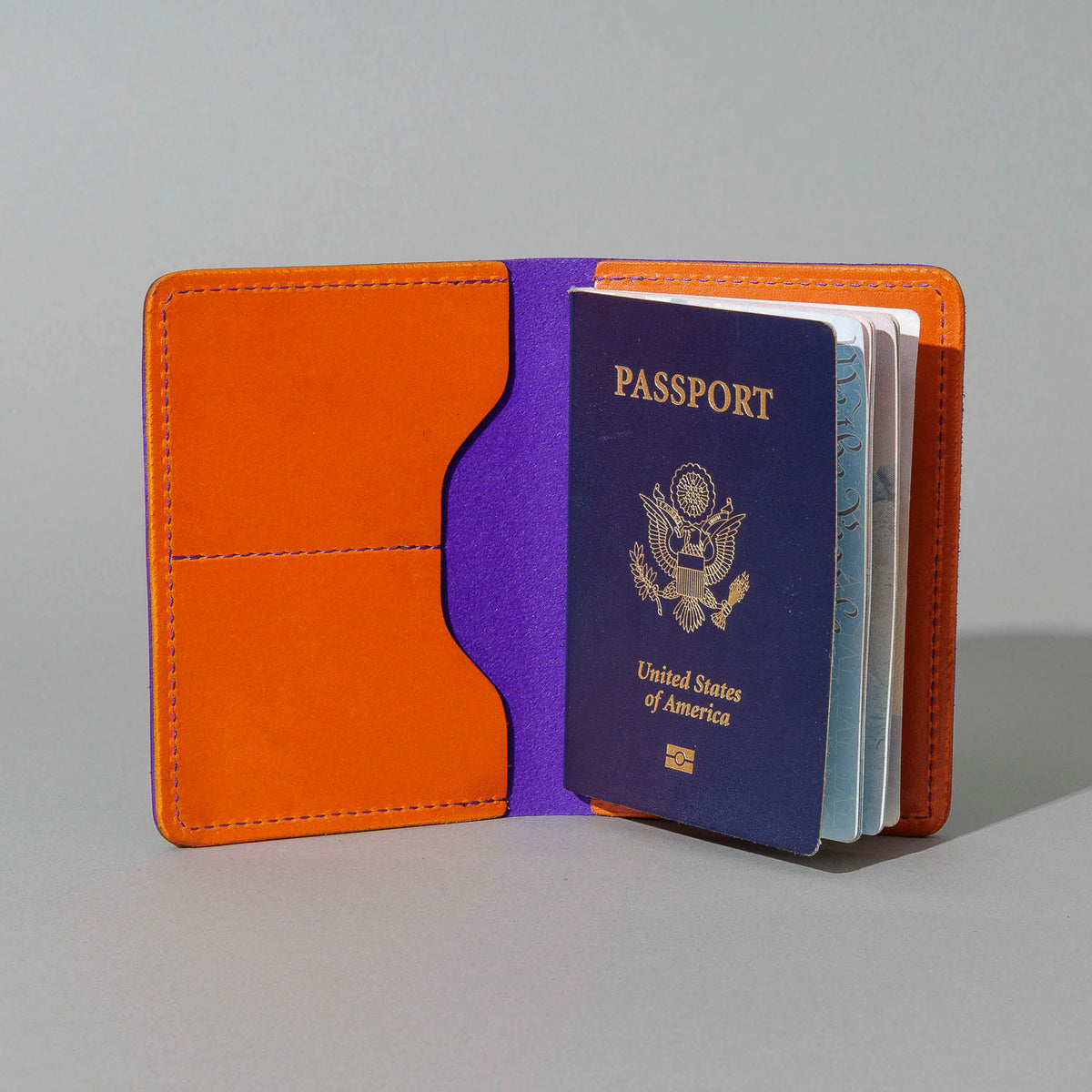 Traveler Passport Holder in Violet Latigo Exterior, Orange Latigo Interior, open with a passport inside