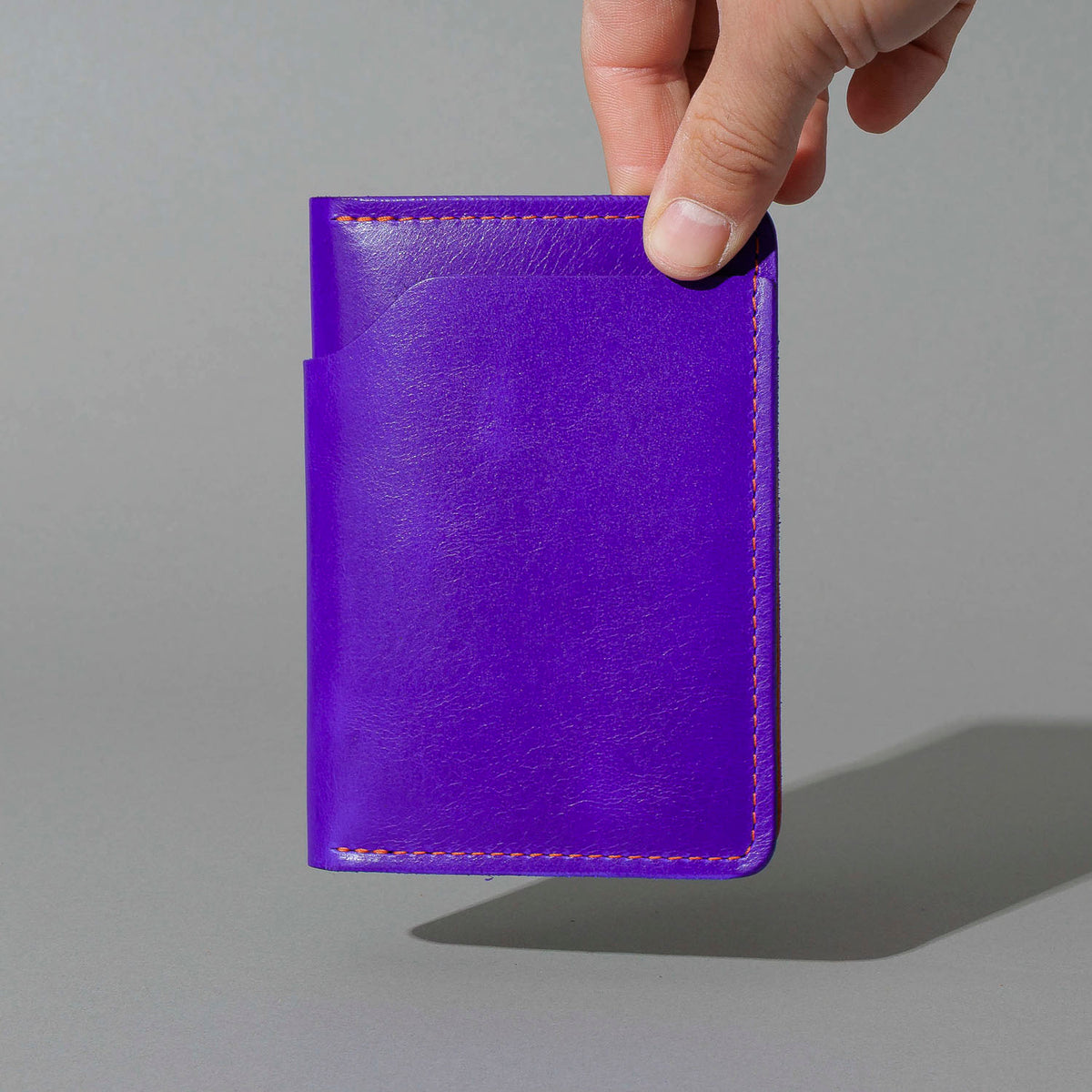 Traveler Passport Holder in Violet Latigo Exterior, Orange Latigo Interior, held in hand, shot 1