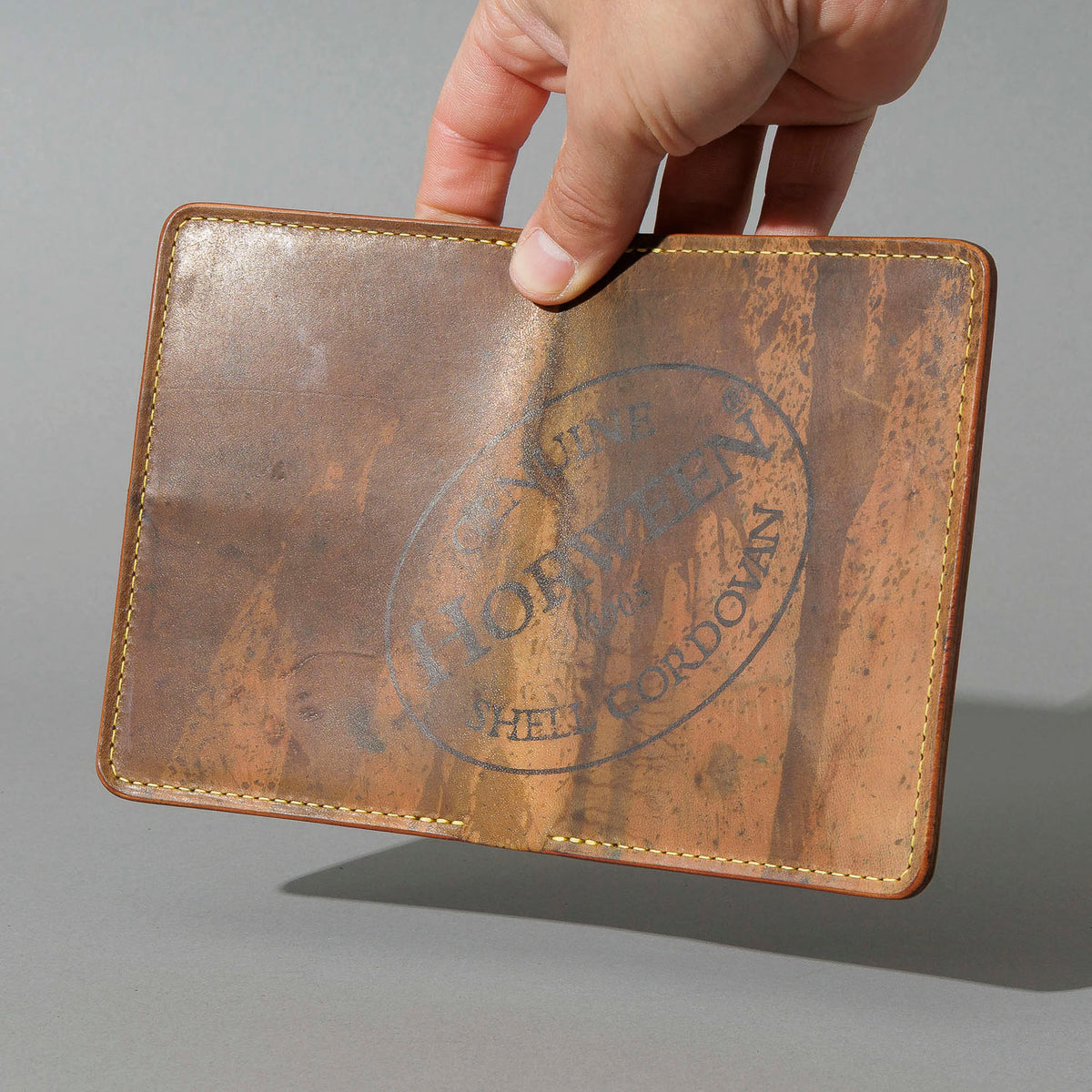 One-Off Traveler Passport Holder in Epic Splatter Reverse Cigar Shell Cordovan, No Bill Slot, held open in hand, shot 1