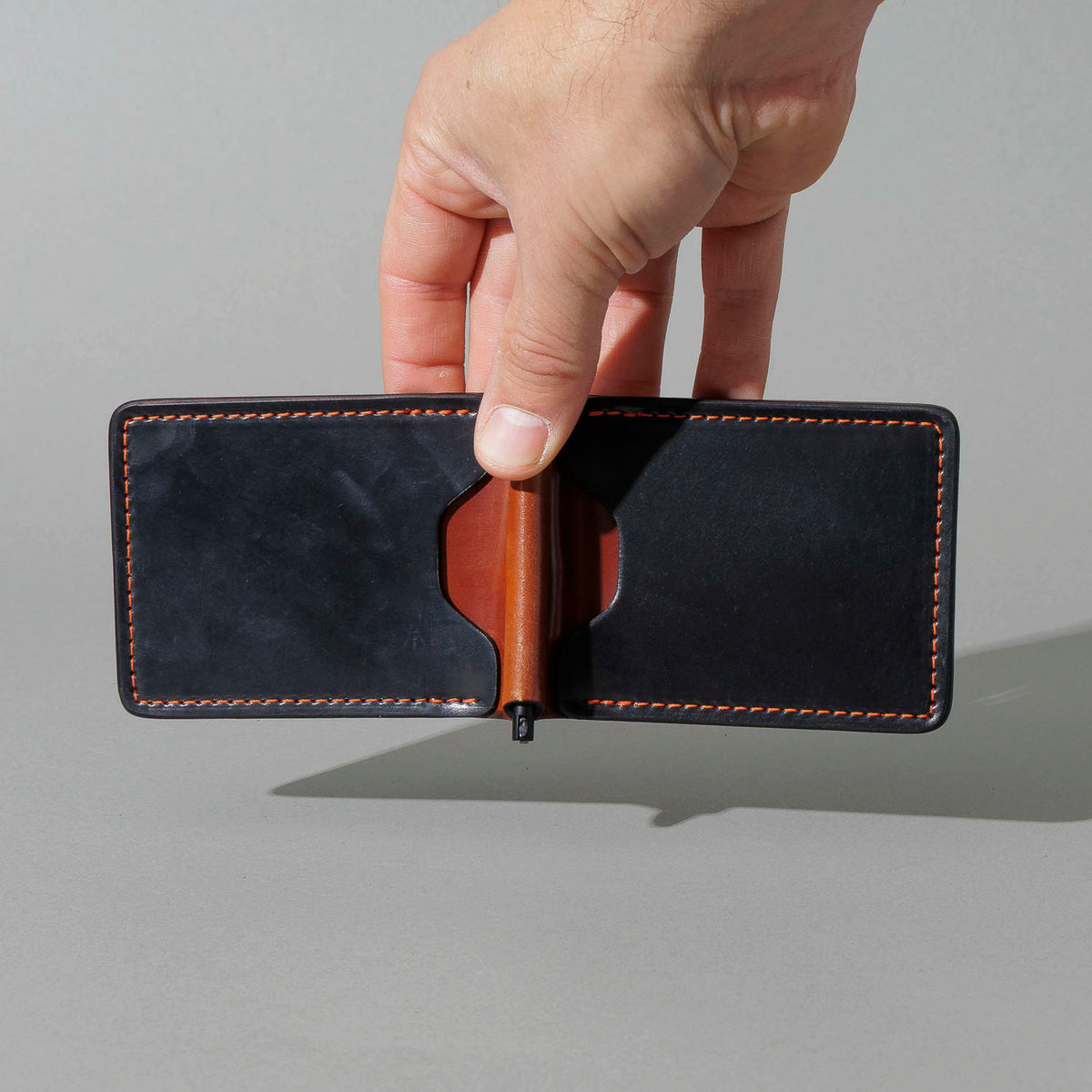 One-Off Capone Money Clip in Black on Blood Orange Shell Cordovan, held open in hand, shot 2