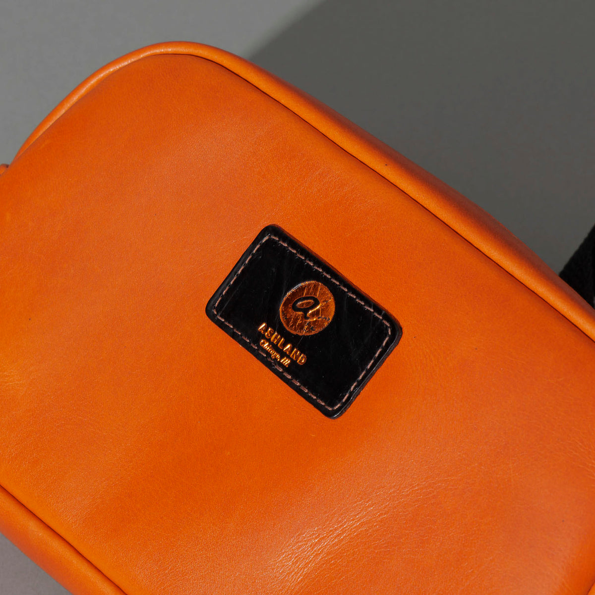 One-Off Sling Bag in Orange Latigo, close-up of the logo patch, shot 1