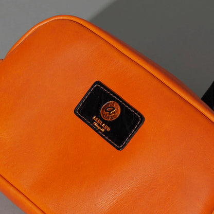 One-Off Sling Bag in Orange Latigo, close-up of the logo patch, shot 1
