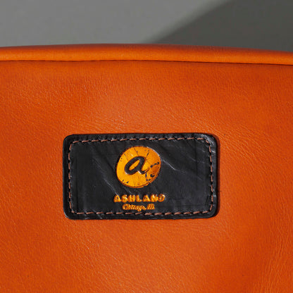 One-Off Sling Bag in Orange Latigo, close-up of the logo patch, shot 2