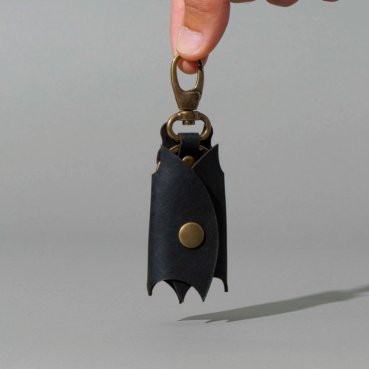 Bat Leather Key Case in Black Dublin, hanging from fingers by the clip, shot 1