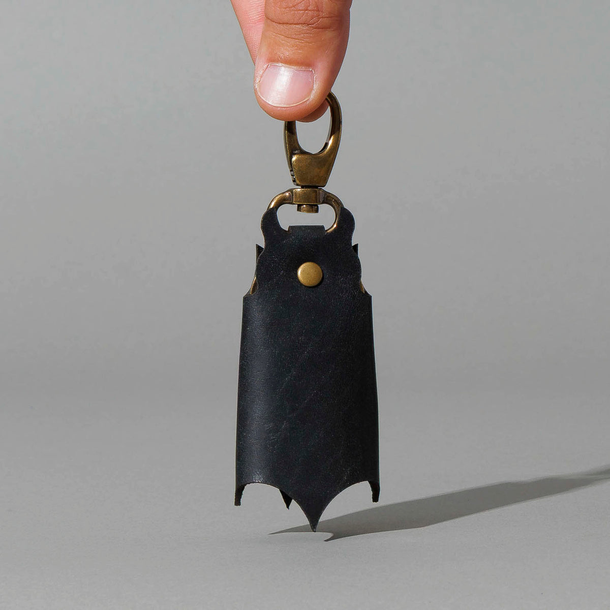 Bat Leather Key Case in Black Dublin, hanging from fingers by the clip, shot 2
