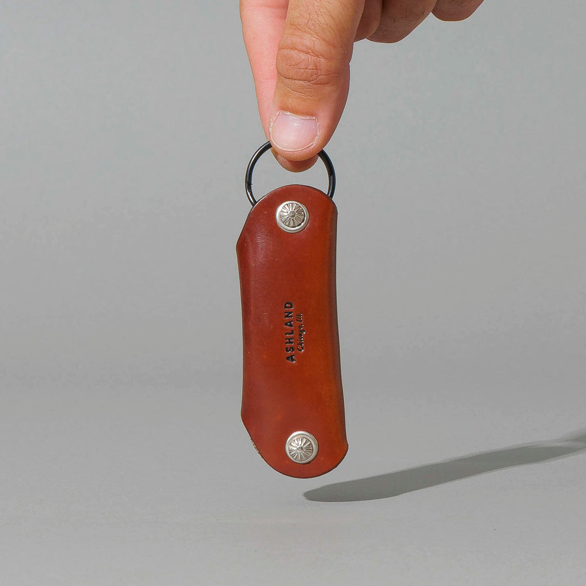 Vault Key Holder in Blood Orange Shell Cordovan, hanging from fingers by the clip, shot 1