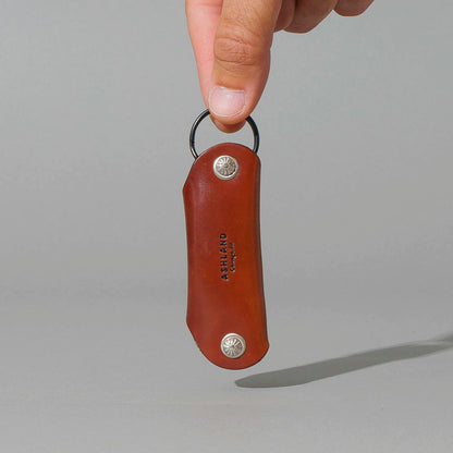 Vault Key Holder in Blood Orange Shell Cordovan, hanging from fingers by the clip, shot 1