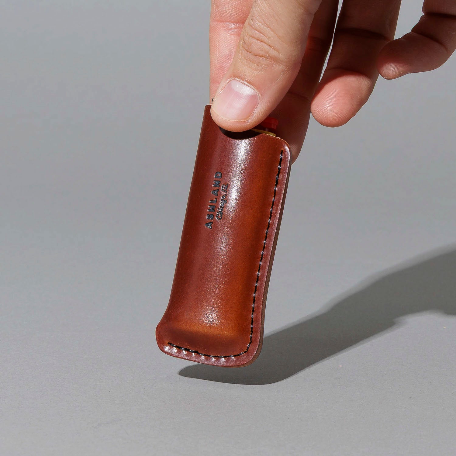 One-Off Lighter in Blood Orange Shell Cordovan, BIC lighter in sheath, held in hand, shot 1