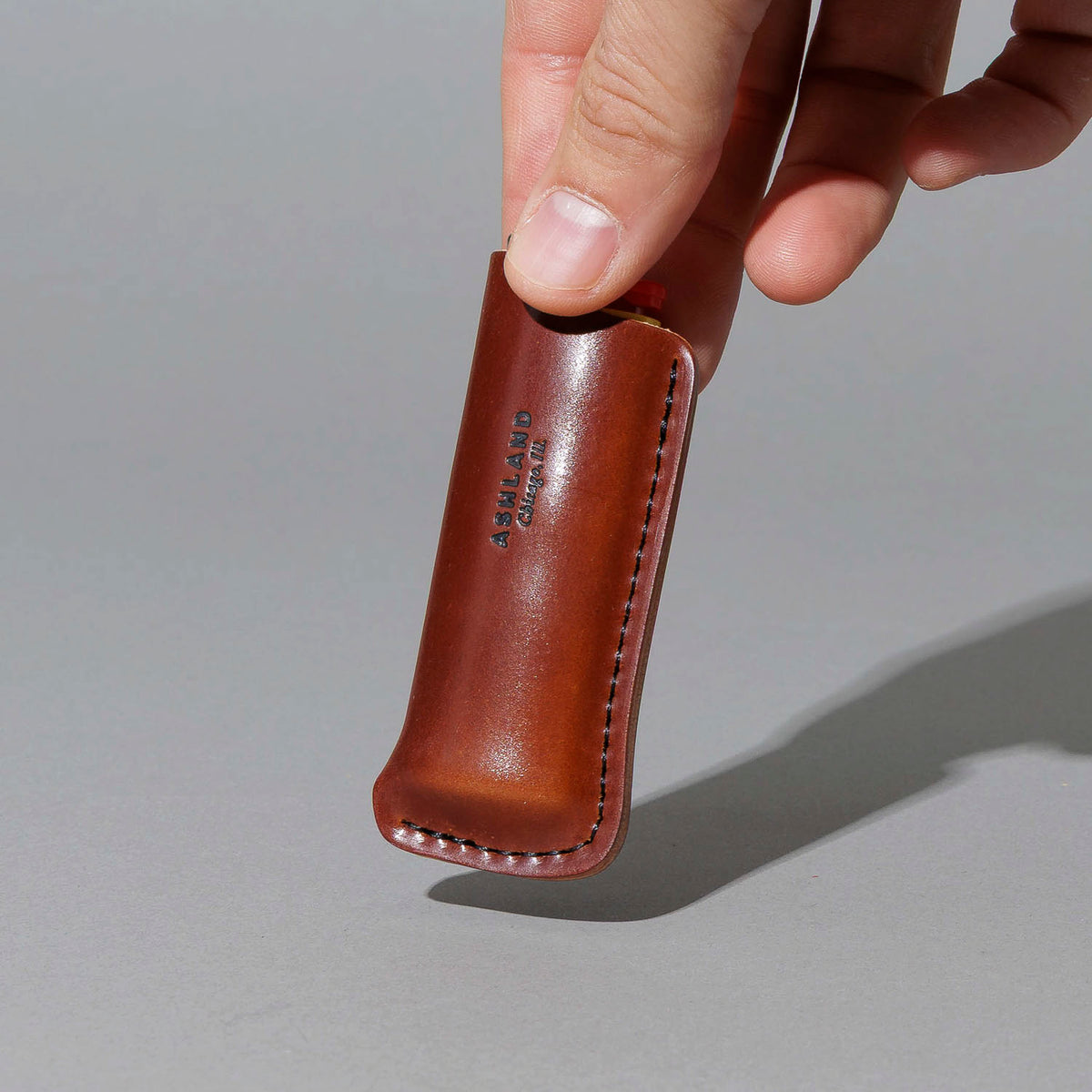 One-Off Lighter in Blood Orange Shell Cordovan, BIC lighter in sheath, held in hand, shot 1