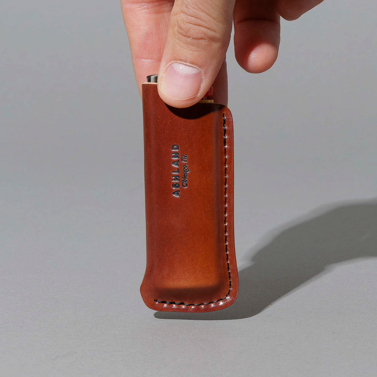One-Off Lighter in Blood Orange Shell Cordovan, BIC lighter in sheath, held in hand, shot 2