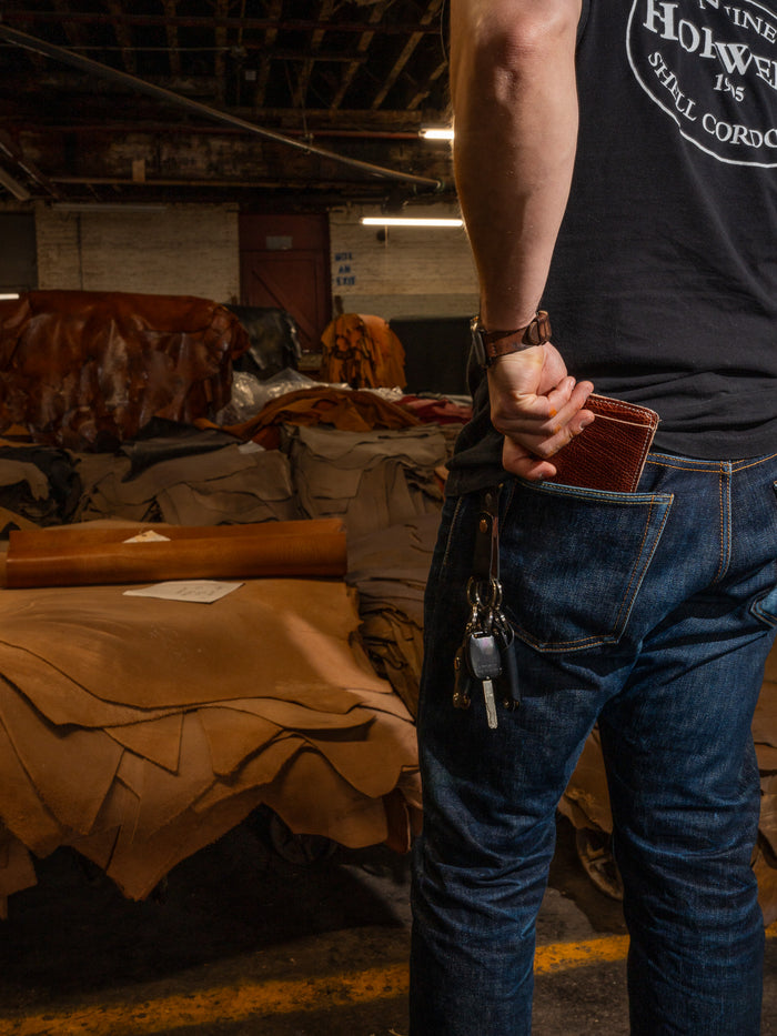 Person holding a leather wallet beside a workbench at the tannery