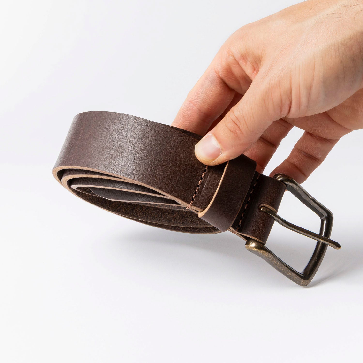 Brown leather belt with a buckle held by a hand on a white background