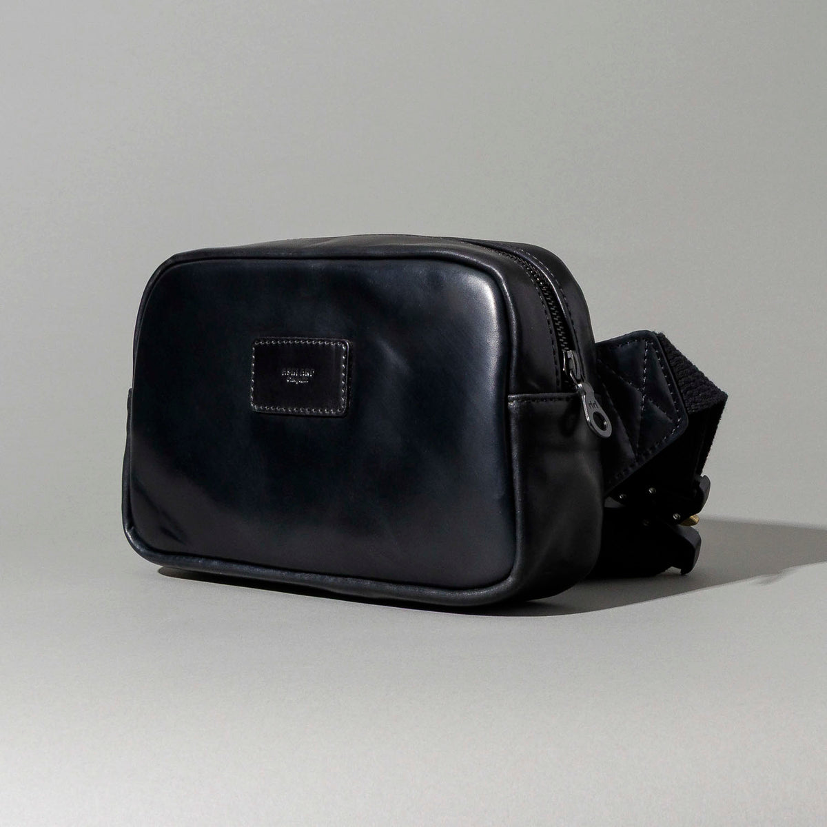 Ashland Leather black Shell Cordovan Sling Bag, front three-quarter view showing brand plaque and adjustable strap