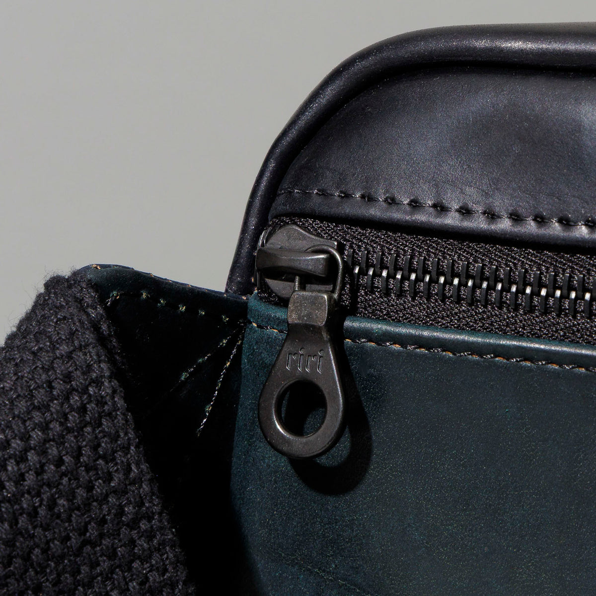 Close-up of the zipper pull and strap attachment point on the Ashland Leather Sling Bag
