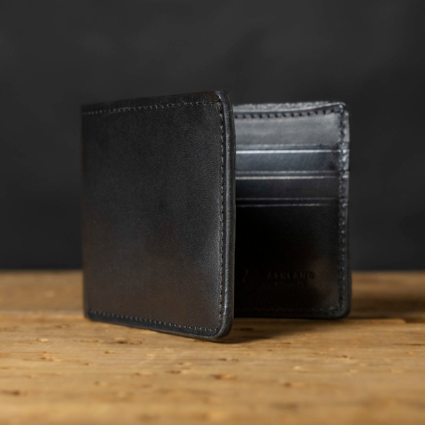 A black bifold wallet made of Horween Dublin leather, displayed on a wooden surface.
