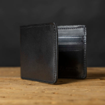 A black bifold wallet made of Horween Dublin leather, displayed on a wooden surface.