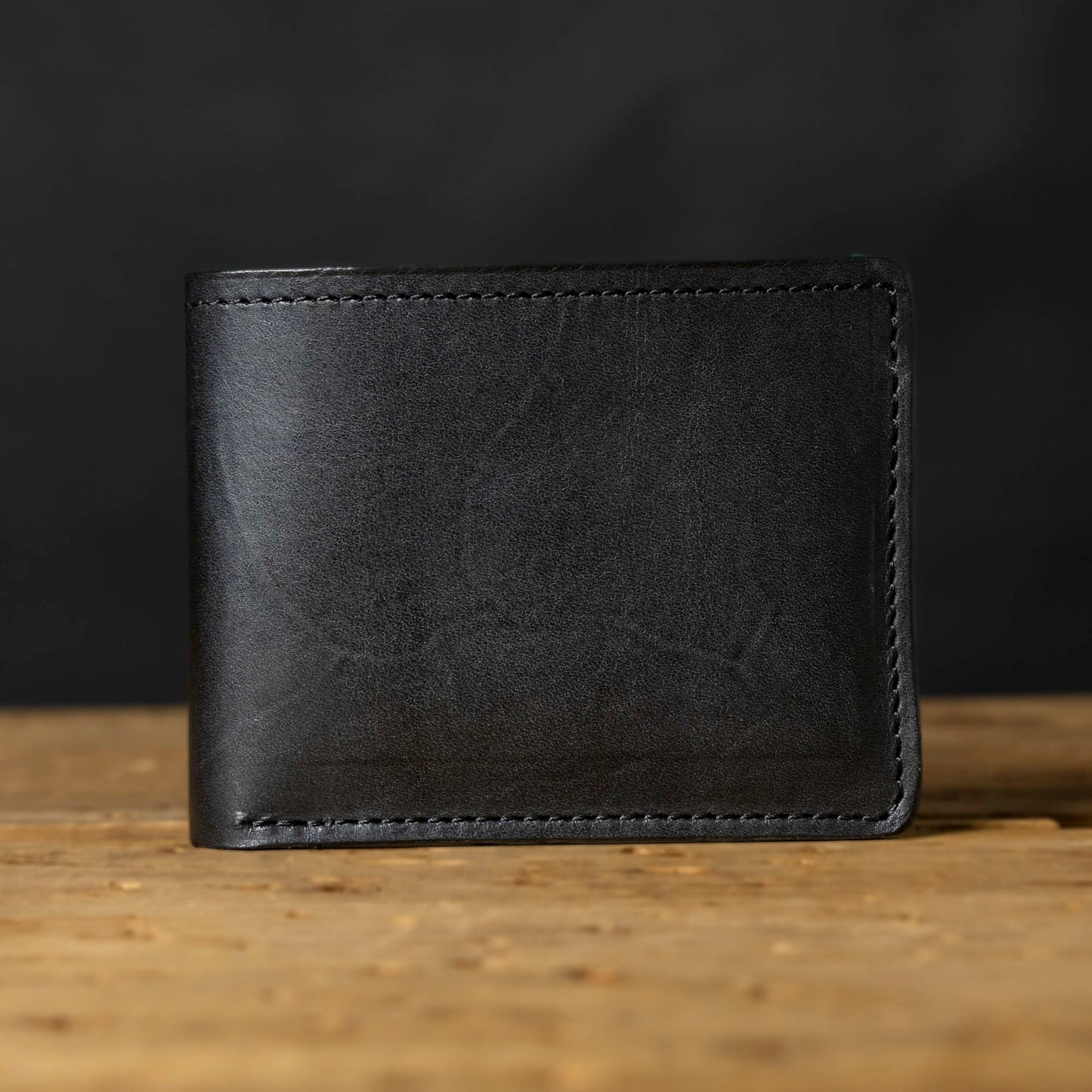 A black bifold wallet made of Horween Dublin leather, displayed on a wooden surface.