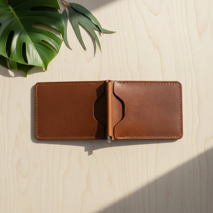 Brown leather wallet open on a light wooden surface with a leaf in the corner