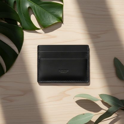 Black leather cardholder on a light wooden surface with green leaves