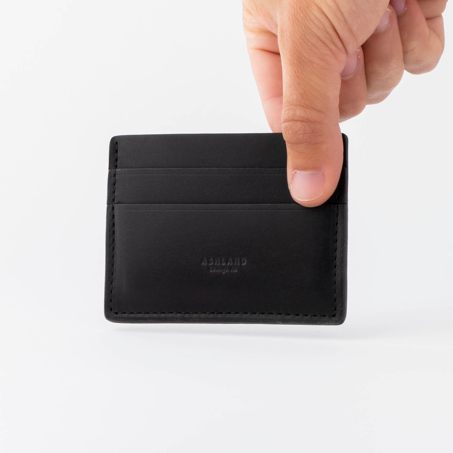 Black leather cardholder with branding held by a hand on a white background