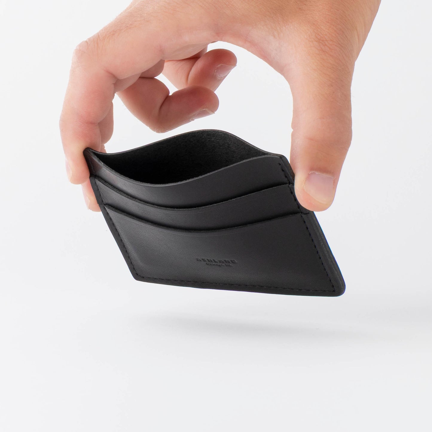 Hand holding a black wallet against a white background to show interior compartment