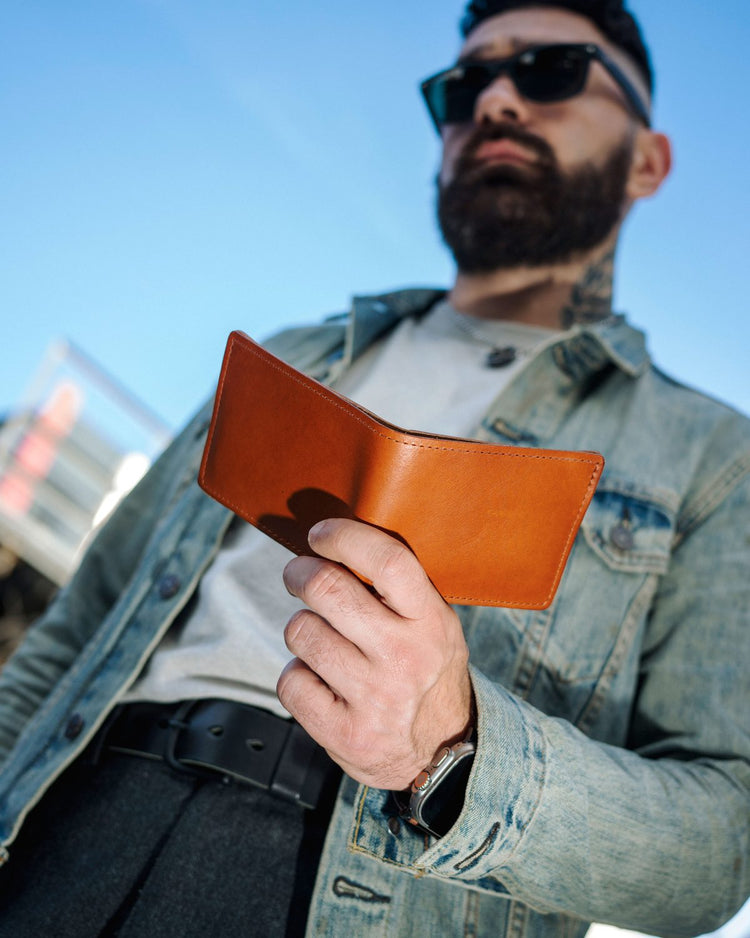 Man in a denim jacket holding a Johnny the Fox bifold wallet in English Tan Horween® Dublin leather under the Chicago L tracks