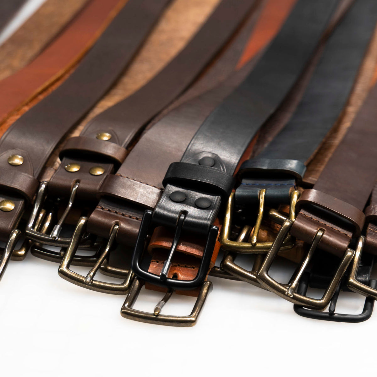 Row of belt buckles in matte black, antique brass and silver tone on assorted leather straps