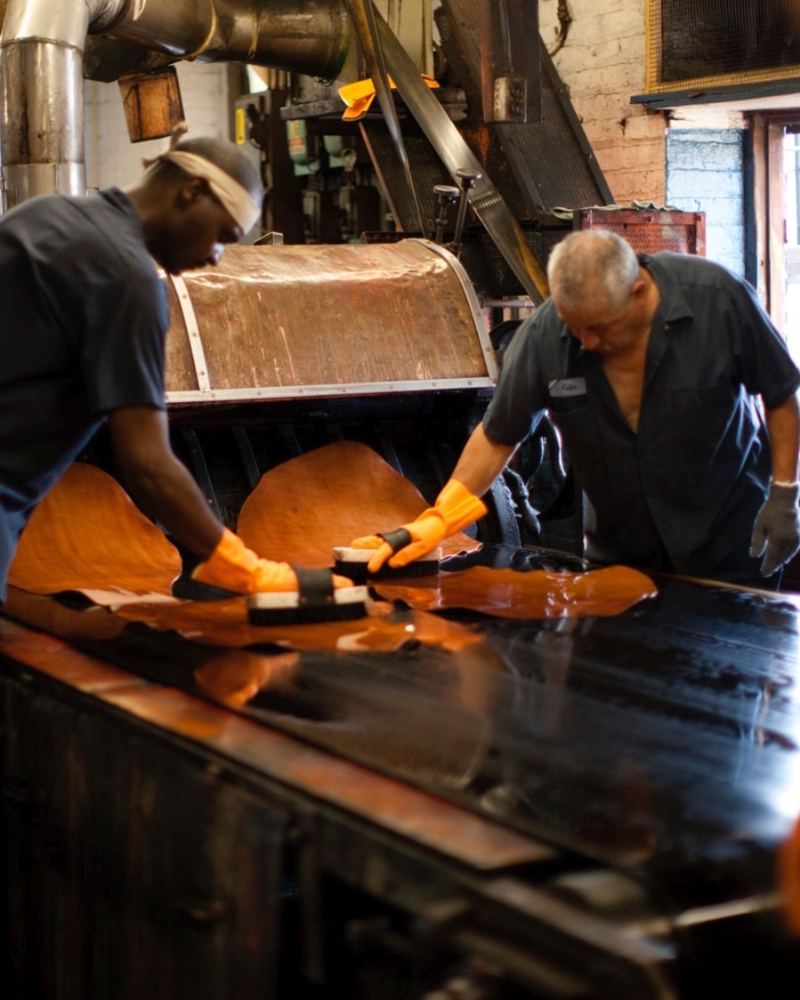 Two workers finishing a hide at a table on the Horween® tannery floor, Chicago