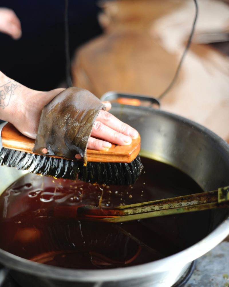 A hand brushing a hide above a pot of dark finish at the Horween® tannery, Chicago