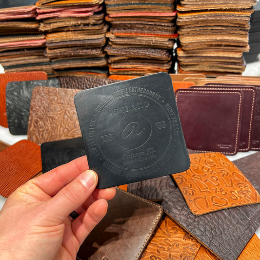 Hand holding a black leather coaster with embossed branding against a background of other Horween leather coasters