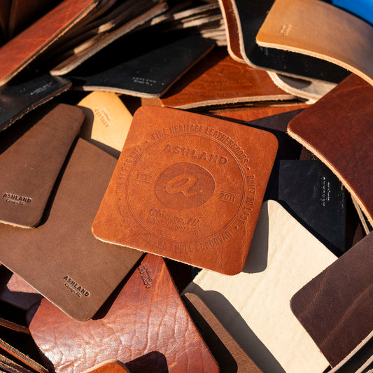 Collection of leather coasters with a visible brand logo on a textured surface.