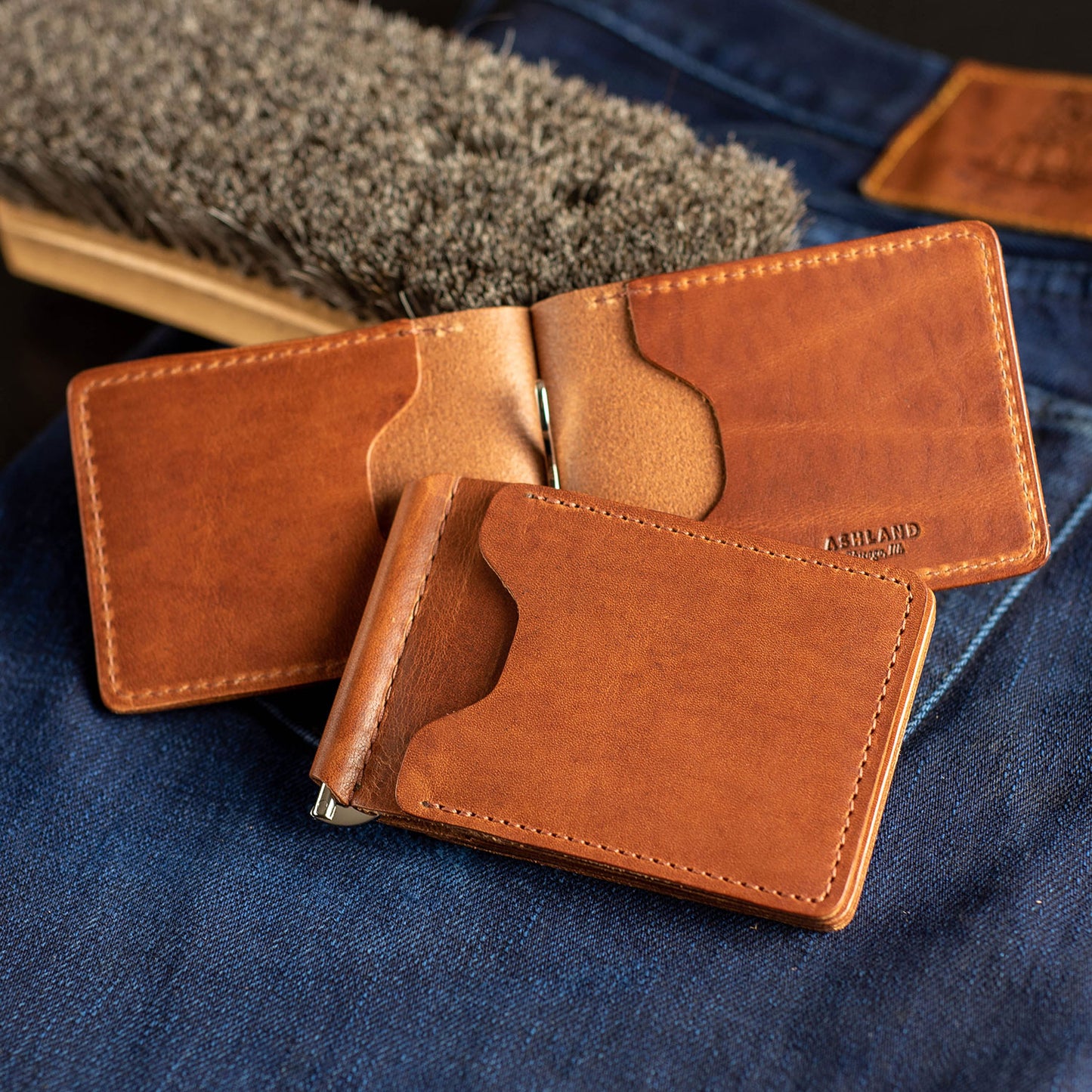 Several Capone Money Clips in English Tan Dublin sitting on blue jeans with a leather care brush